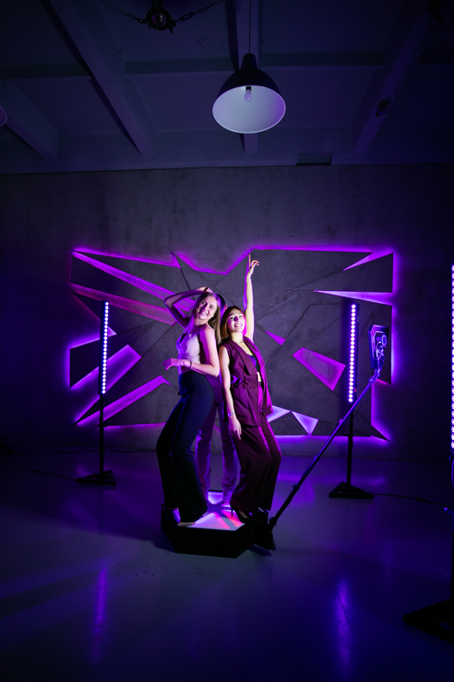 Two guests posing on the orbit 360 photo booth platform as the camera arm sweeps around them under purple event lighting