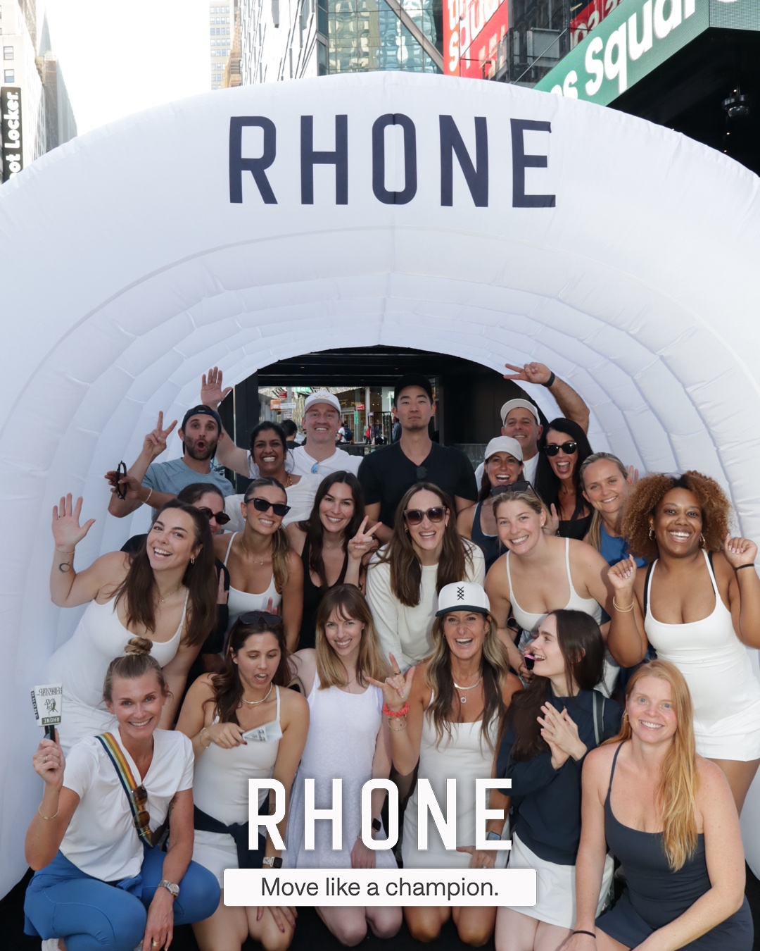 A large group posing inside the branded Rhone tunnel with a 'Move like a champion.' overlay, Times Square NYC