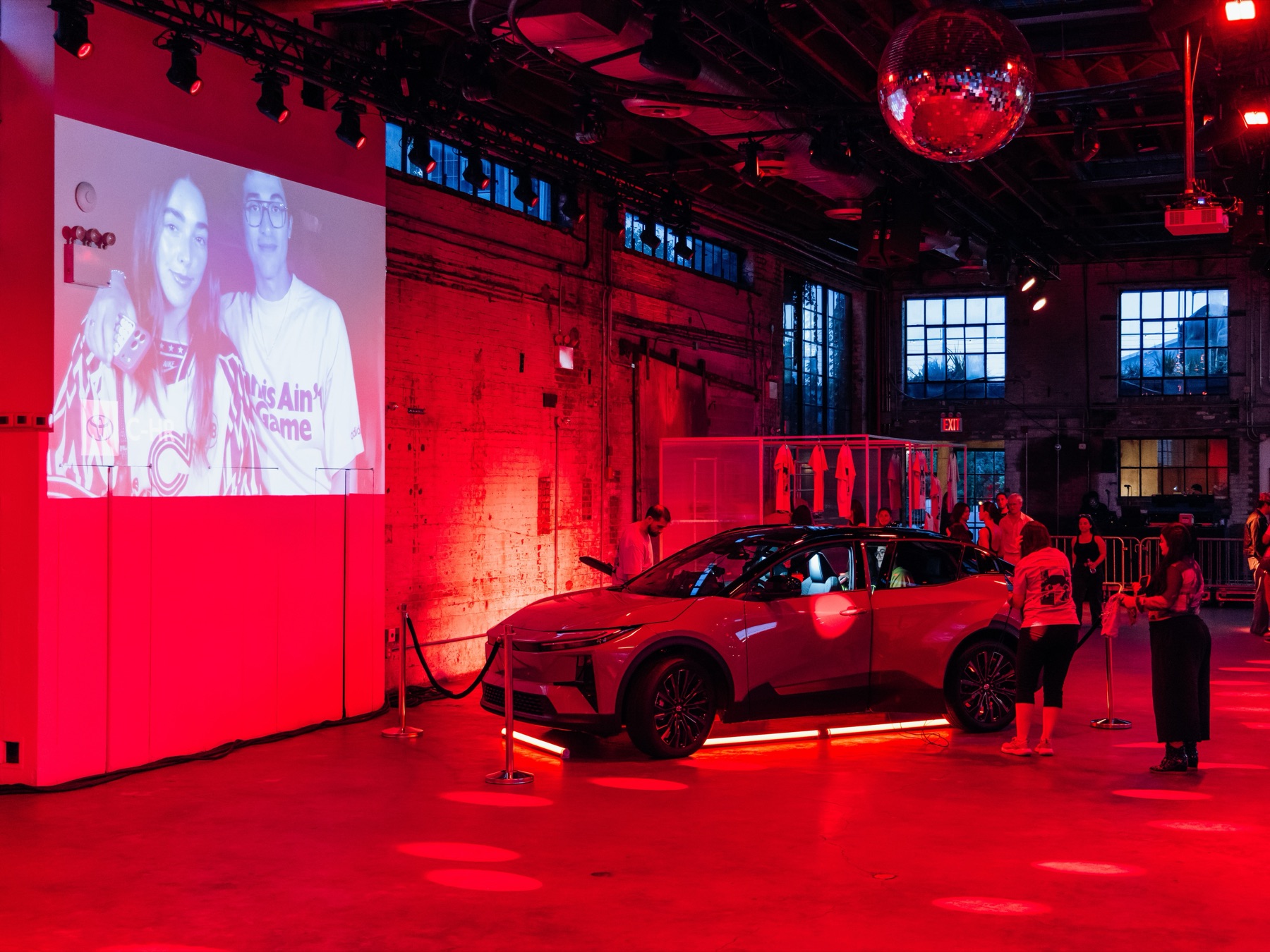 The in-car camera livestream projected large on the venue wall showing two guests, with the Toyota C-HR and crowd gathered below