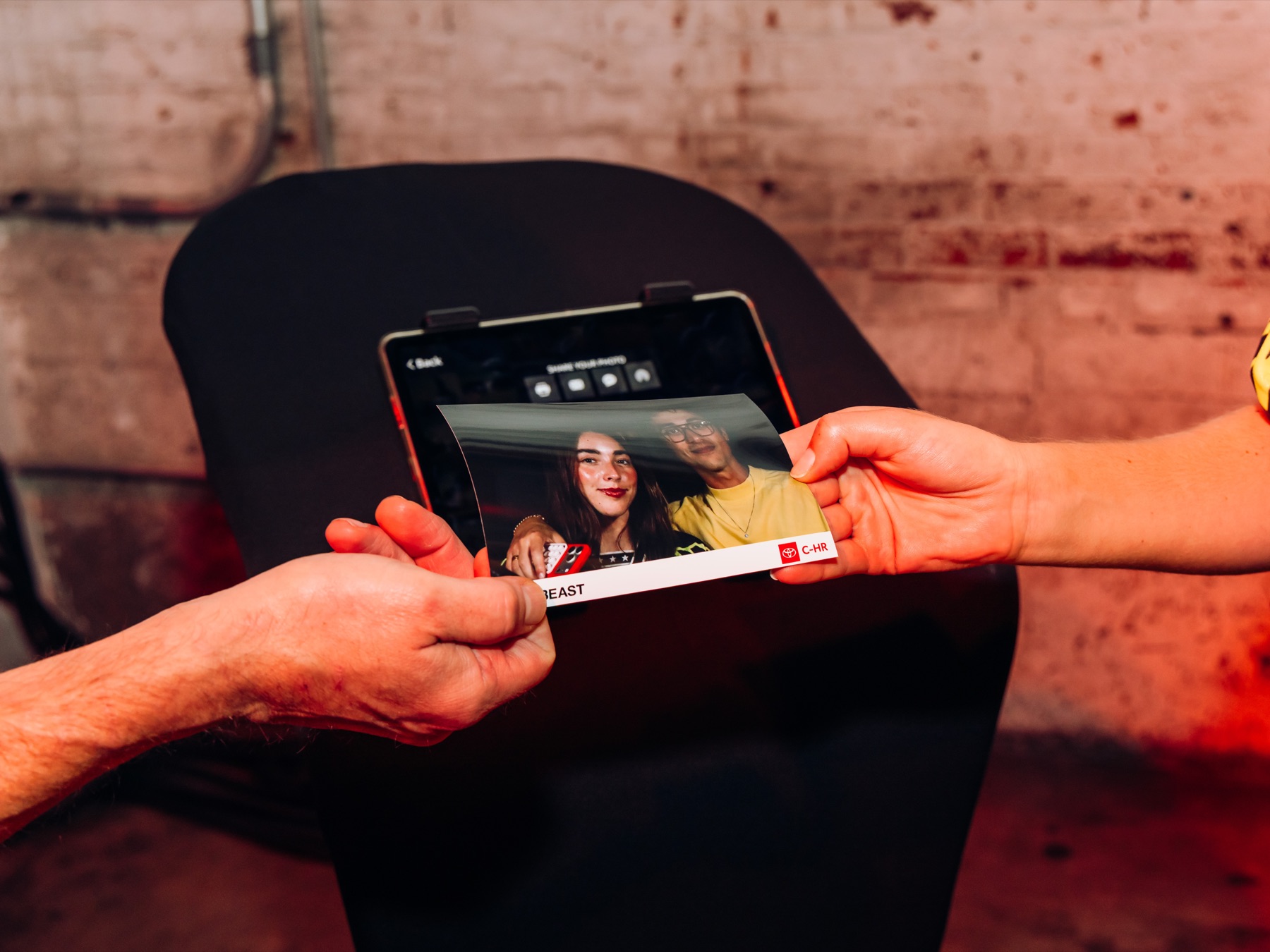 Hands passing an iPad showing a guest's finished photo from the in-car camera rig, branded with the Hypebeast x Toyota C-HR logo