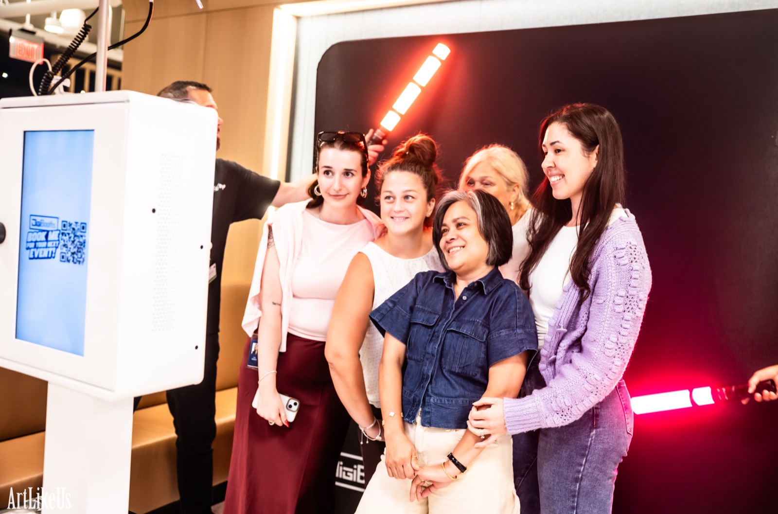 Behind the scenes at the DigiBooths light painting booth — five guests posing while an operator sweeps a glowing red LED wand behind them
